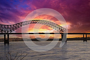 A shot of the flowing water of the Mississippi river with a stunning blue, yellow and red sunset in the sky with a bridge