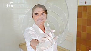 Shot of focused syringe. Blurred young female doctor in white uniform. Portrait of a Happy smiling female beautician in