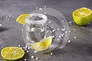 Shot glass with tequila, salt and lime slices on a gray