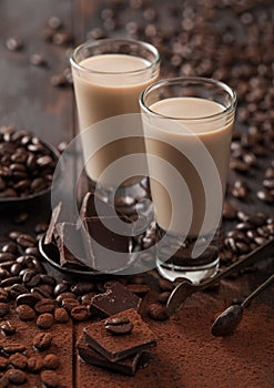 Shot glasses of Irish cream baileys liqueur with coffee beans and powder with dark chocolate on dark wood background