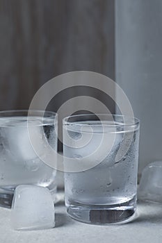 Shot glasses of vodka with ice cubes on light grey table