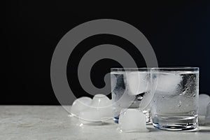 Shot glasses of vodka with ice on light grey table against black background. Space for text