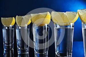 Shot glasses of vodka with lemon slices on blue background