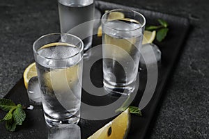 Shot glasses of vodka with lemon slices, mint and ice on grey table