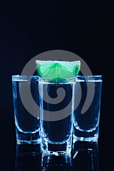 Shot glasses of vodka with lime slice on dark background