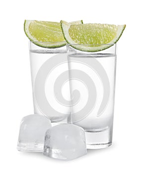 Shot glasses of vodka with lime slices and ice on white background