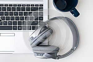 Shot of a gray headphone on a gray laptop next to a blue mug isolated on a white background