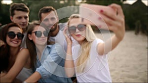 Shot of a group of young friends taking a selfie on the beach. Men and women taking photos sitting on a sand on warm