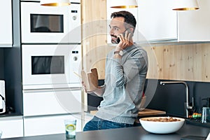 Handsome mature business man eating take away noodles while using smartphone in the kitchen at home