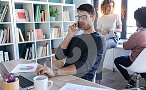 Handsome young entrepreneur talking on mobile phone while working with laptop in the office