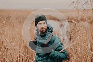 Shot of handsome young man with dark stubble, carries backpack, looks back, notices something, has thoughtful expression, spends