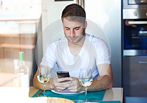 Handsome young man using his mobile phone in the kitchen at home.