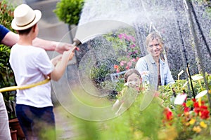 Happy boy playing with hose and wetting his mother and sister. photo