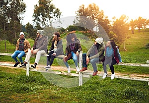 Getting out of the city for the weekend. Shot of a happy group of friends sitting in a row on a fence together.