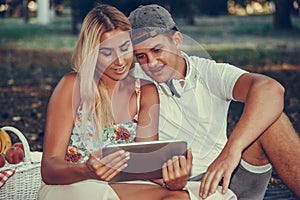 Shot of a happy young couple looking at a tablet while having a picnic