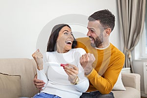 Shot of a happy young couple taking a pregnancy test at home. A Happy excited woman making positive pregnancy test and celebrating