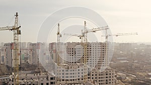 Shot in height of several yellow construction cranes and construction of new buildings for housing and office in the