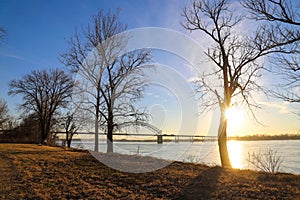 A shot of the Hernando de Soto Bridge over the flowing waters of the Mississippi river with a blue sky at sunset