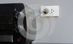 Shot image of black mini electric oven with plugin outlet power at wall background