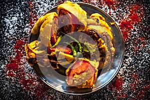 Shot of Piyaz pakora/bhaji/bhajji/bhajiya/bajji in a glass plate with some fresh green chilies and red chili powder along with it photo