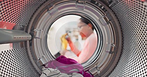 Shot from inside washing machine drum, woman opens door and packs colorful clothes inside, puts t-shirts, jeans in wash