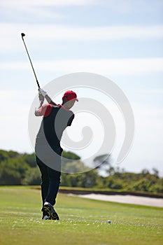 The shot isnt finished until you follow through. Rear view shot of a man in mid golf swing.