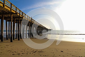 A shot of a long winding brown wooden pier at the beach with silky brown sand and vast blue ocean water