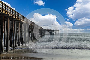 A shot of a long winding brown wooden pier at the beach with silky brown sand and vast blue ocean water