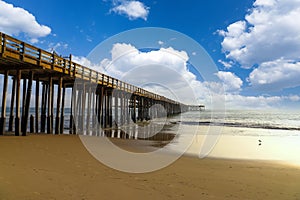 A shot of a long winding brown wooden pier at the beach with silky brown sand and vast blue ocean water