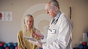 Shot of a male senior doctor discussing records with young female patient at rehabilitation center