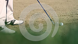 Shot of a man golfer on a sand golf course hitting the white golf ball with