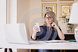 Shot of middle aged woman using mobile phone and text messaging while working from home