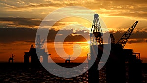 Shot of offshore oil platforms in the water over sunset sky. Large drilling oilfields with cranes extracting crude oil