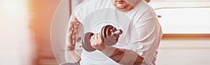 Shot of Overweight tattooed man training with dumbbell at gym with sunlight