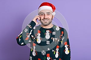 Shot of positive Christmas man talking via modern smart phone. Bearded man in Santa hat speaking on cell phon, handsome male
