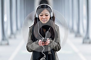 Pretty asian young woman listening to music with her smartphone in the street.