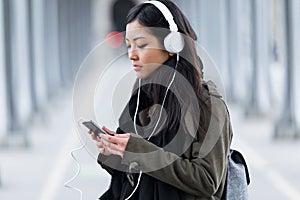 Pretty asian young woman listening to music with her smartphone in the street.