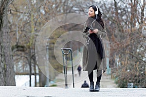 Pretty asian young woman listening to music with her smartphone in the street.