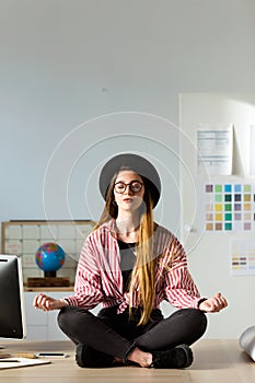 Pretty young business woman doing yoga on the table in the office.