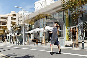 Shot of pretty young woman in dress crossing the street while holding the take away coffee and looking sideways