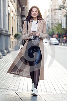 Pretty young woman looking at camera while listening to music with her mobile phone in the street