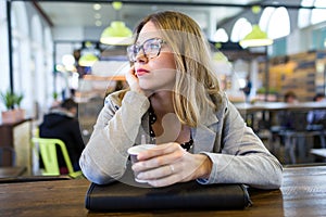 Pretty young woman looking sideways while drinking cup of coffee at cafe. photo