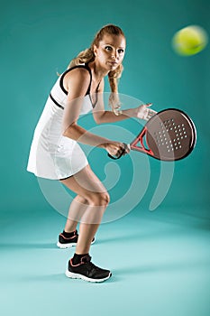 Pretty young woman playing padel indoor over green-blue background. photo