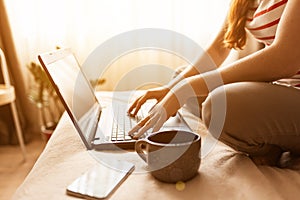 Shot of pretty young woman using her mobile phone while working with laptop sitting on the floor at home.