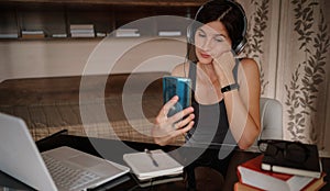 Shot of pretty young woman using her mobile phone while working with laptop sitting at home