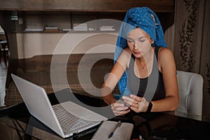 Shot of pretty young woman using her mobile phone while working with laptop sitting at home