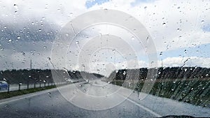 A shot of raindrops that flow down the windshield of a car that rides on the autobahn in rainy weather.