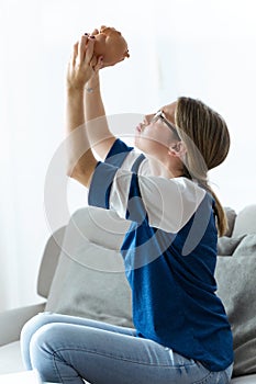 Sad young woman looking and holding her piggy over her head on sofa at home