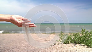 A shot of sand particles falling from a woman`s hands on a sunny beach