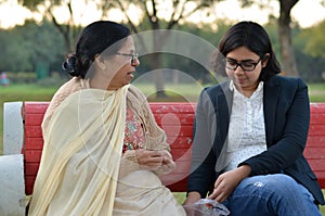 Shot of a senior retired Indian woman sitting in a park with her daughter in law on a red bench peeling peanuts, and eating them.